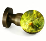 A resin door knob featuring a miniature landscape motif and emitting a warm yellow glow, mounted on a round, copper-toned brass base.