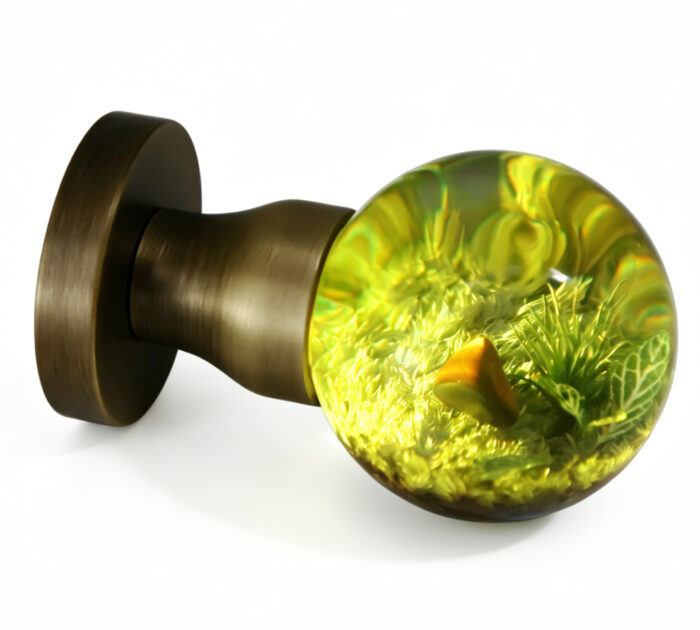 A resin door handle with a miniature landscape theme, illuminated by a warm yellow light. A resin door knob featuring a miniature landscape motif and emitting a warm yellow glow, mounted on a round, copper-toned brass base.