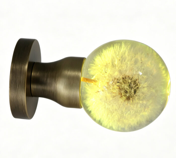A dandelion-themed resin door handle featuring warm yellow illumination. A dandelion-themed resin door knob emitting a warm yellow glow, mounted on a round, copper-toned brass base.