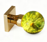 A resin door knob featuring a miniature landscape and emitting a warm yellow glow, mounted on a square gold-tone brass base.
