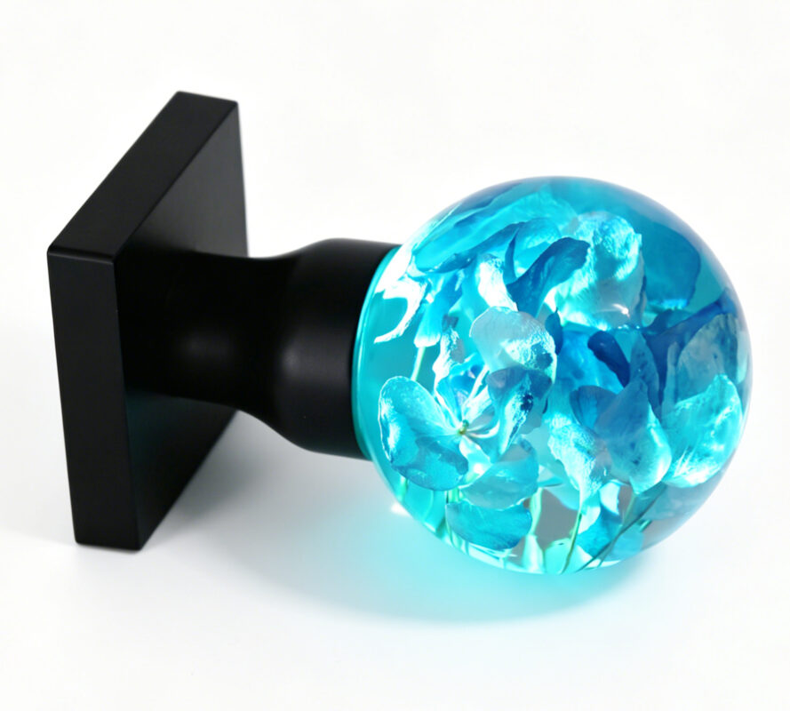 Handcrafted resin door knob featuring hydrangeas that emit a cyan glow, mounted on a square black brass base.