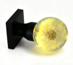 Dandelion resin door knob emitting a warm yellow glow, mounted on a square black brass base